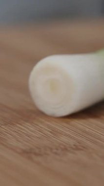 Dikey video. Bir kadın kesme tahtasındaki pırasanın kökünü kesiyor ve kesiyor. Hem de yakından..