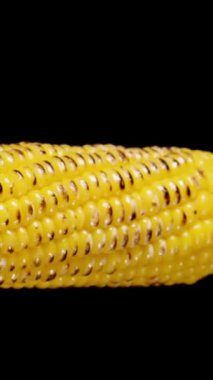 Dikey video. Hafif kömürleşmiş çekirdekli haşlanmış mısır koçanı yan tarafından görülüyor. Kaydırıcı