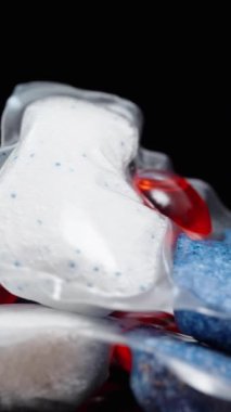 Dikey video. Bulaşık makinesi için kapsüller. İçinde toz ve kırmızı jel olan çözünebilir paketler. Siyah bir arkaplan üzerinde döndürme.