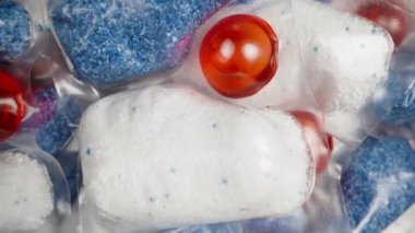 Bulaşık makinesi tozuyla tek bir çözünebilir paket alıyorum, kapsül dönerken kamera yukarı kalkıyor, yakın plan..