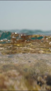 Dikey video. Kamera denizin kenarındaki bir kayanın üzerinde duruyor, ve dalgalar üzerini süzüyor, yavaş çekimde, yakın çekimde.