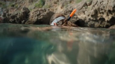 Maske takan ve şnorkel kullanan genç bir kadın sualtı dünyasını gözlemliyor. Suyun altındaki manzara resife baktığını gösteriyor..