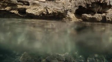 Su altından deniz kayalıklarının panoramik bir görüntüsü, iki perspektifi yakalar: suyun üzerindeki ve altındaki uçurumlar..