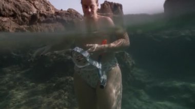 Genç bir kadın kayalıklardaki açık deniz suyunda elinde bir şnorkel maskesiyle su altında solunum tüpüyle duruyor..