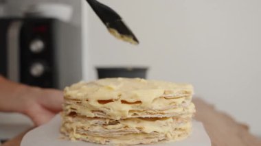 Pasta şefi kremayı pasta katmanlarının arasına eşit bir şekilde yaymak için siyah spatula kullanır ve Napolyon keki yapar..