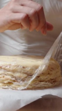Dikey video. Pasta şefi Napolyon 'un pasta tabanından plastik ambalajı kaldırıyor..