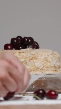 Dikey video. Bir kadın Napolyon pastasını kirazlarla süslüyor, yavaş çekimde yan gözle..