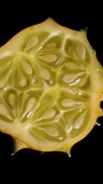 Dikey video. Siyah arka planda dönen dilimlenmiş bir Kiwano salatalığı. İçindeki et ve tohumları gösteriyor..