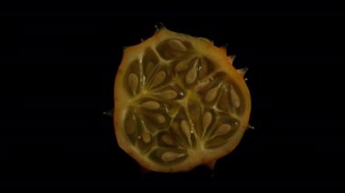 Kesilmiş Kiwano salatalığı siyah arka planda dönüyor, yavaş yavaş gölgeye dönüşüyor..