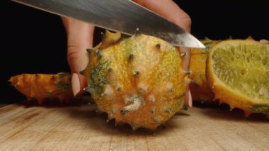 Dikenli Kiwano ikiye bölünürken kamera da yaklaşıyor. Masada bir Afrika salatalığı var. Yakın çekim, yumuşak hareket.