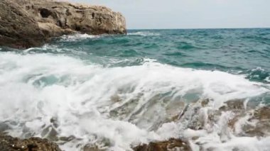 Kıyı kayalarına köpükle vuran azgın deniz ve turkuaz dalgalar.