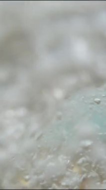 Dikey video. Kamera bir kayaya çarpan okyanus dalgalarını yakalıyor, tamamen suya gömüyor, ve sonra denize geri çekiliyor. Yavaşça yaklaş.