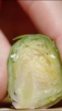 Dikey video. Beyaz manikürlü bir kadın eli Brüksel lahanasını sıkıyor ve meyve suyu yavaşça içinden damlıyor..