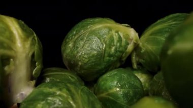 Bir yığın pişmiş Brüksel lahanası, kamera geriye doğru hareket ederken ve bir kadın üste birkaç tane daha eklerken.