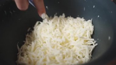 Ağır çekimde bir kadın, rendelenmiş peyniri mavi kasede çatalla karıştırıyor..