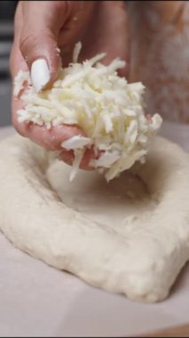 Dikey video. Kadın Khachapuri Lobio 'yu hazırlıyor, Gürcistan usulü bir peynirli ekmek. Hamuru rendelenmiş peynirle dolduruyor..