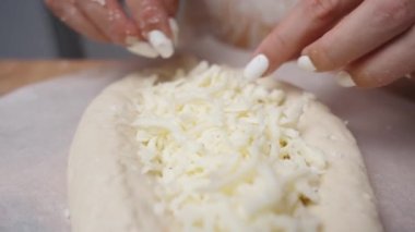 Kadın, Adjaran tarzı Khachapuri 'ye rendelenmiş peynir dağıtmak için ellerini kullanıyor. Sahne yavaş çekimde çekiliyor, yakın çekimde gösteriliyor..