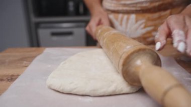 Genç bir kadın büyük bir tahta oklavayla masanın üzerine hamur atıyor ve sahne ağır çekimde çekiliyor..