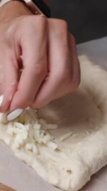 Dikey video. Kadın Adjarian Khachapuri yapıyor, rendelenmiş peyniri hamura sarıyor..