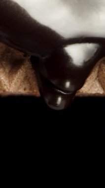 Dikey video. Siyah arka planda çikolata damlayan waffle dokusu. Kaydırıcı atışı, makro.