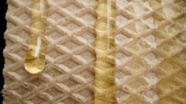 Bal damlaları, waffle 'ın dokusuna siyah bir zemin üzerinde damlar, yakın çekim kaydırma görüntüsü.