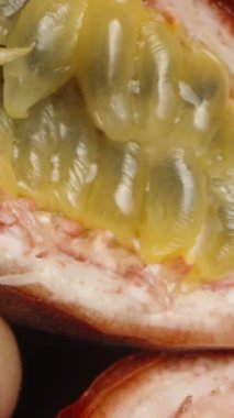 Dikey video. Tutku meyvesinin yarısını sıkıyorum ve suyu diğer yarısına damlıyor. Kamera aşağı doğru hareket ediyor. Makro çekim.