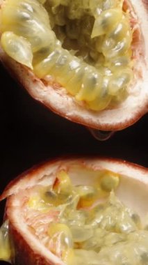 Dikey video. Dilimlenmiş tutku meyvesi, siyah arka planda iki yarım, damlacıklar damlıyor..