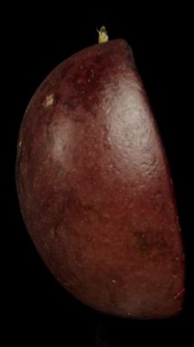 Dikey video. Tutkulu bir meyvenin yarısı siyah bir zemin üzerinde döner ve içinde tohumlar olan tarafını gösterir. Yakın plan çekim. İzole edilmiş.