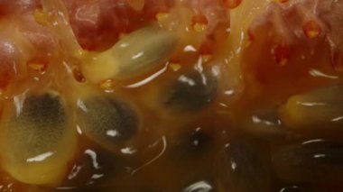 İçinde çekirdek kalıntıları olan tutku meyvelerinin yarısı siyah arka planda döner ve kameradan uzaklaşır, makroyu izole eder..