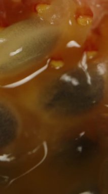 Dikey video. İçinde çekirdek kalıntıları olan tutku meyvelerinin yarısı siyah arka planda döner ve kameradan uzaklaşır, makroyu izole eder..