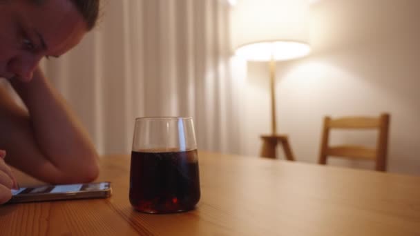 一个孤独的年轻女人 在昏暗的灯光下 喝着威士忌和可乐 翻阅着她的手机 — 图库视频影像