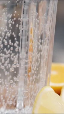 Dikey video. Yukarı doğru hareket ediyor, masaya limon ve portakal dilimleri dökülüyor, gazoz bardağa dökülüyor.