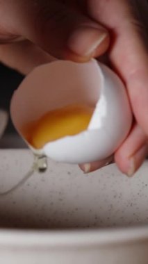Dikey video. Bir kadın yumurtanın beyazını kabuğun içindeki sarıdan ayırır. Yavaş çekimde, yakın çekimde..