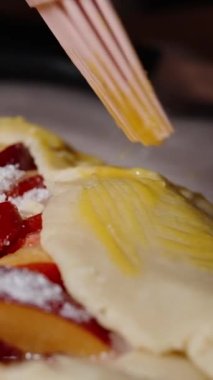 Dikey video. Nektarin turtasını çırpılmış yumurtayla silikon fırçayla fırçalıyorlar..