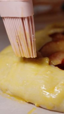 Dikey video. Şeftalili turtanın kenarları fırçayla fırçalanarak altın bir kabuk oluşturulur..