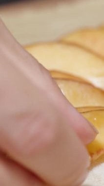 Dikey video. Bir kadın hamur üzerinde bir daire şeklinde nektarin dilimleri düzenler, yavaş çekimde yakın çekimde..