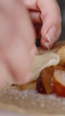 Dikey video. Bir kadın şeftalili turta yapmak için hamurun kenarlarını katlıyor..