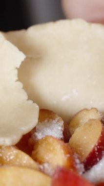 Dikey video. Kadın hamuru şeftalilere sarıp turta yapıyor. Yakın çekim..