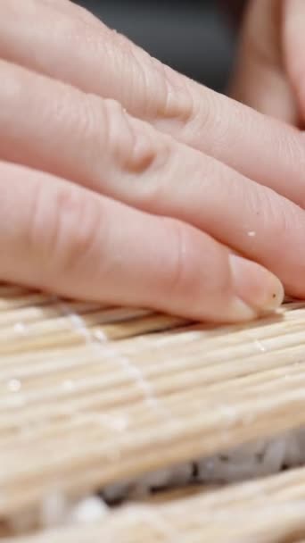 バーティカルビデオ 女性は竹マットで寿司ロールを転がします — ストック動画