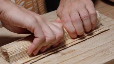 Kadın bambu hasırı kullanarak suşiyi yuvarlıyor ve sıkıca bastırıyor..