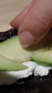 Dikey video. Avokado dilimleri Norveç yosunlarının üzerindeki krem peynirin üzerine konur..