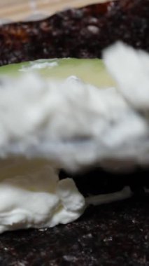 Dikey video. Krem peynir, avokado, nori yosun çarşafları ve suşi rulolarının üzerine yayılır..