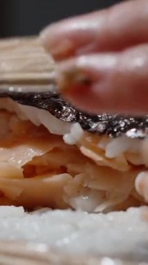 Dikey video. Kadın, içinde somon parçaları olan suşiyi yuvarlıyor, yakın plan..