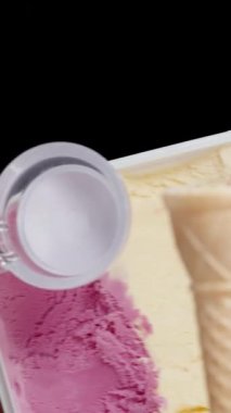 Dikey video. Pembe tonda bir dondurma kabı ve siyah bir arka planda izole edilmiş waffle külahının içine atmak için bir kaşık..