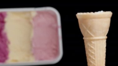 Boş bir waffle külahı ve siyah arka planda çok renkli pembe bir dondurma kabı..