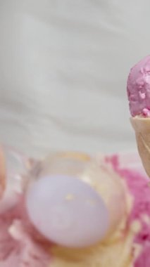 Dikey video. Bir kadın waffle külahındaki pembe kepçenin üstüne ikinci bir kepçe dondurma koyar. Yakın plan..