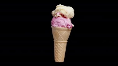 İki dondurma toplu bir waffle külahı, biri pembe diğeri krema renkli, siyah arka planda dönüyor. İzole görünüm.