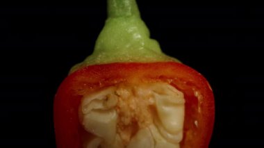 İçinde tohumlar olan yarım biberiye kırmızısı biber, aşağı düşme simülasyonu yaparak siyah bir zemin üzerinde döner. Makro yakınlaştırma. İzole görünüm.
