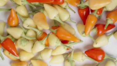 Mini kırmızı biber karışımı beyaz bir masaya ağır çekimde serpiştirilir, üst görüntüden çekilir..