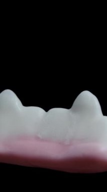 Dikey video. Beyaz dişler ve vampir dişleri şeklinde bir şeker, siyah bir arka planda dönüyor, izole edilmiş, yakın planda..